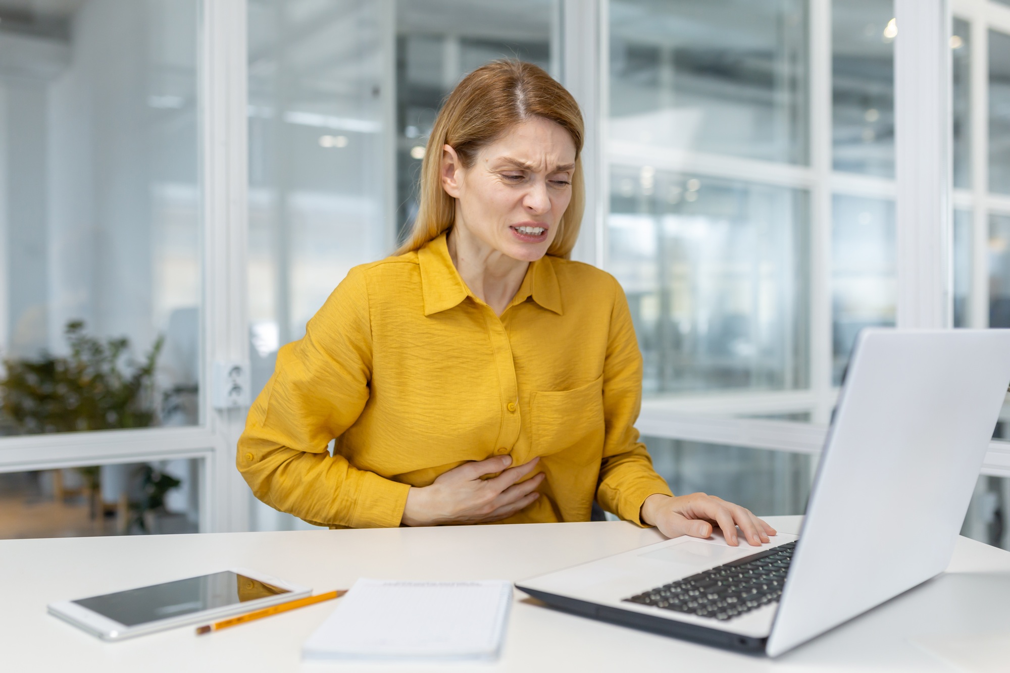 Woman experiencing stomach pain while working on a laptop in an office